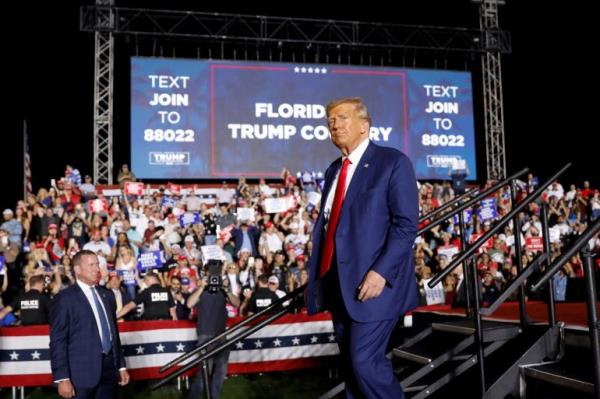 Trump, in a blue suit and red tie, walks down a me<em></em>tal staircase in front of a crowd of supporters, who cheer in front of a sign that reads: 
