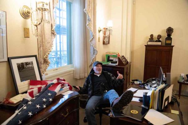 One of the rioters sitting at Pelosi's desk in the Capitol building.