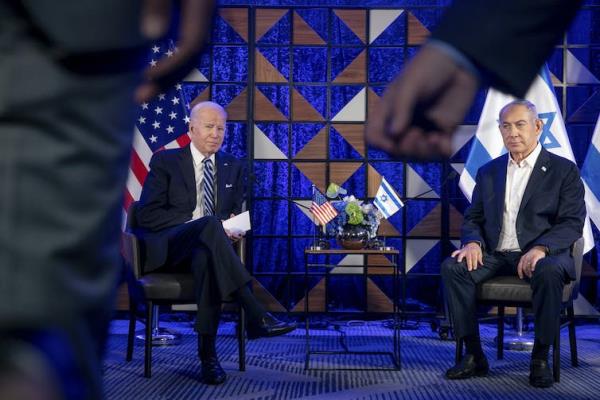 Two men in suits sit in seats in from of a blue backdrop