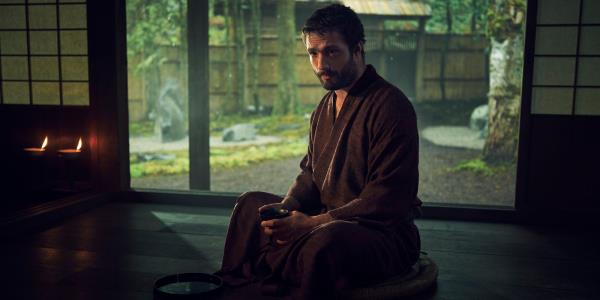 John Blackthorne sits on the flooring holding a cup in Shogun