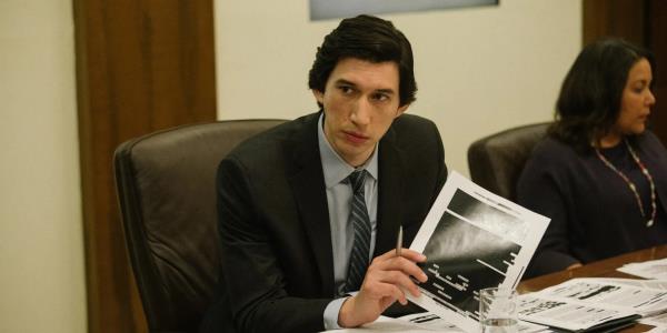 Adam Driver at a co<em></em>nference table, holding a heavily redacted docu<em></em>ment in The Report