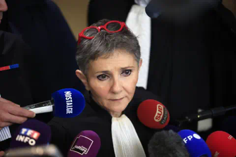 EPA Béatrice Zavarro with grey hair and red-rimmed glasses on her head stands in front of several micropho<em></em>nes as she speaks to the press.